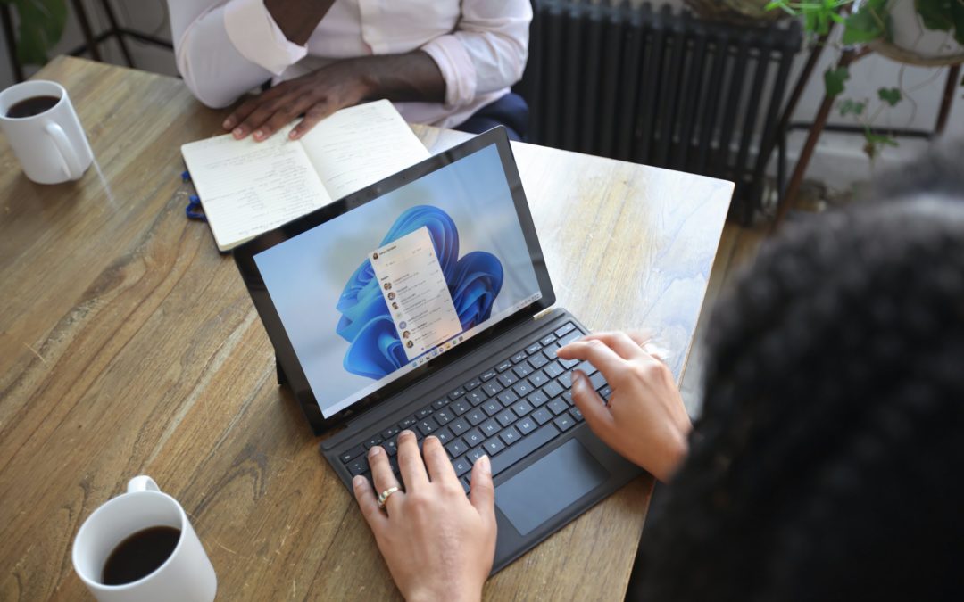 Overhead view of two people at a table working with a Microsoft laptop and notebook