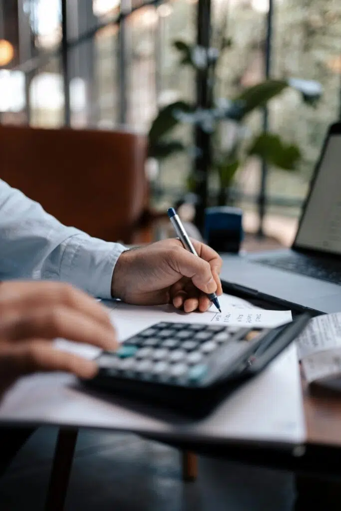 Free A person calculating finances with a calculator and pen on a desk indoors. Stock Photo