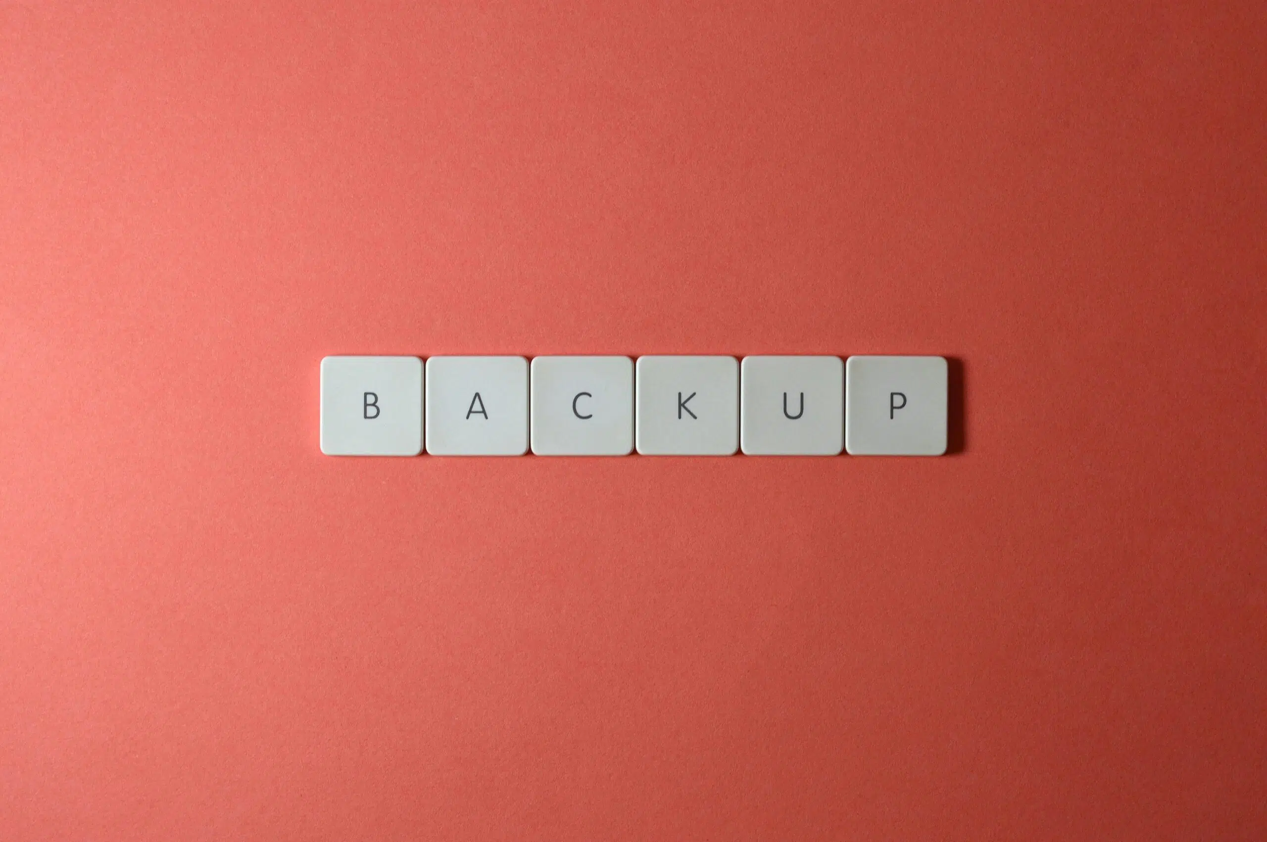 Free Close-up of keyboard keys spelling 'BACKUP' placed on a coral-colored surface. Stock Photo